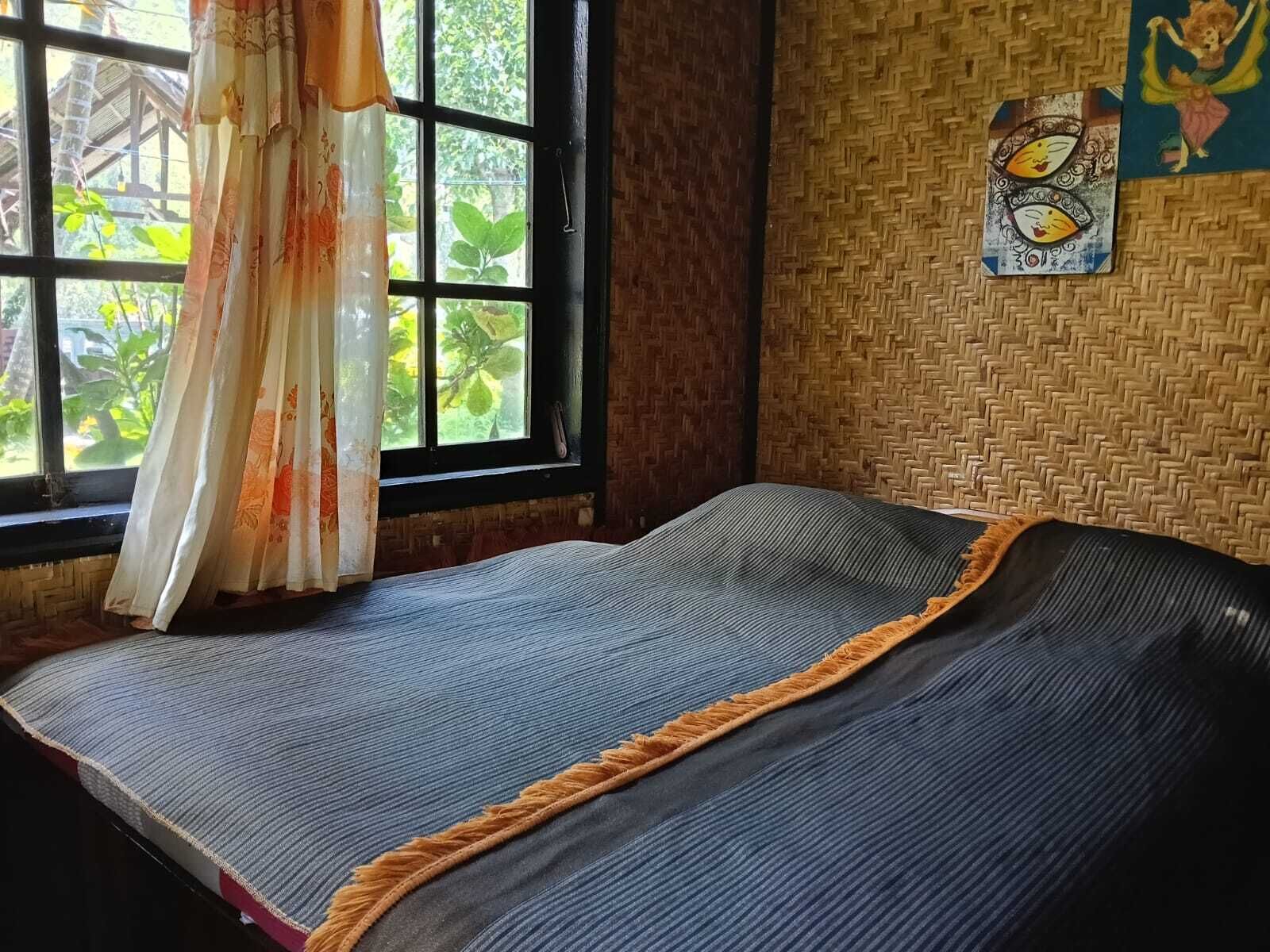 A room with a bed, a window with curtains, a woven wall, and a wall decoration.