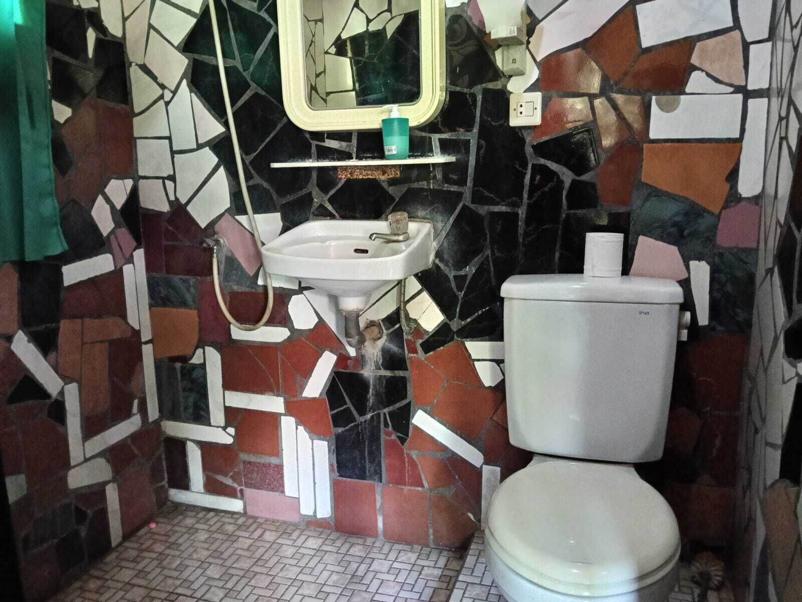 Une salle de bain avec un mur recouvert de mosaïques, un lavabo blanc et des toilettes.