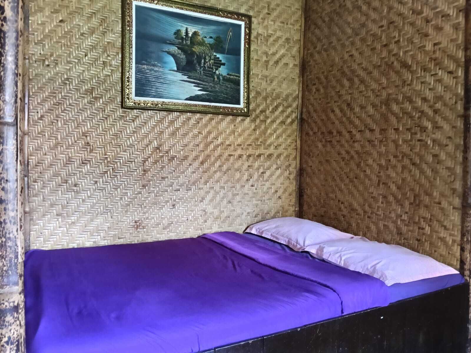 A room with a bed, a woven wall, and a framed picture.