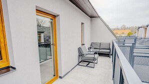 A balcony with a glass door, a sofa, and a chair. - Rezidence Petra Voka 208 by Interhome (Trebon)