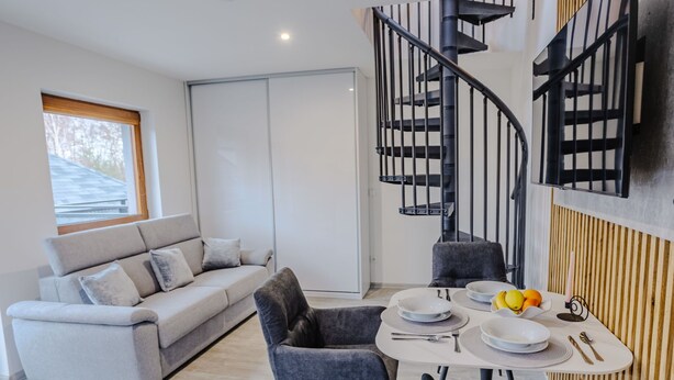 A modern living room with a sofa, dining table, and a spiral staircase. - Rezidence Petra Voka 208 by Interhome (Trebon)