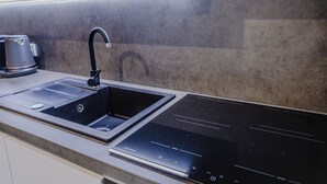 A modern kitchen with a black sink, a coffee maker, and a sleek induction cooktop. - Rezidence Petra Voka 208 by Interhome (Trebon)