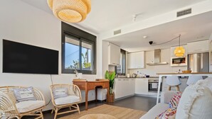 A modern living room with a flat-screen TV, wicker furniture, and a large window.