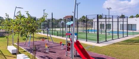 Un parque infantil con un tobogán rojo, columpios y una cancha de baloncesto.