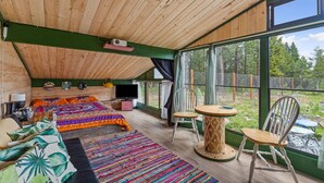 Une pièce chaleureuse avec un plafond en pente, une grande fenêtre, un lit avec une literie aux couleurs vives, une télévision et un coin repas avec des chaises.