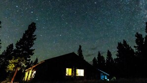 Une cabane avec un ciel étoilé au-dessus, entourée de grands arbres.