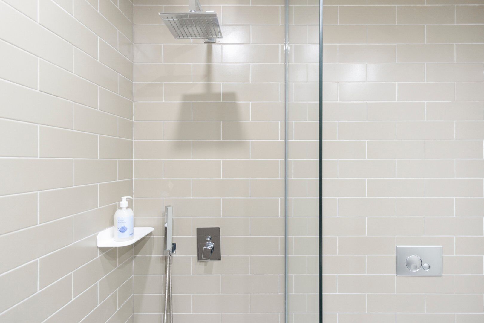 Une salle de bain moderne avec une douche à parois de verre, un lavabo blanc doté d’un distributeur de savon et un panneau de commande pour la douche.