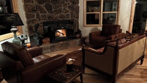 A cozy living room with a stone fireplace, leather furniture, and a wooden coffee table. - House of The Rising Sun (Bailey)
