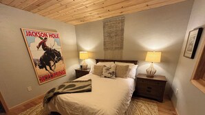 A bedroom with a large bed, two bedside tables with lamps, a poster on the wall, and a patterned rug. - House of The Rising Sun (Bailey)