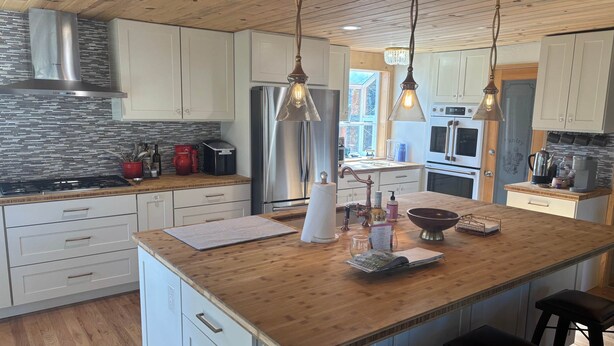 A modern kitchen with wooden ceiling, stainless steel appliances, and pendant lighting. - House of The Rising Sun (Bailey)