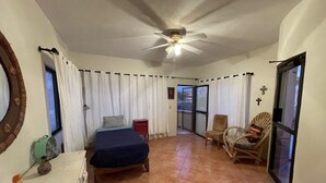 Quarto com cama, uma cadeira, mesinha e ventilador de teto.
