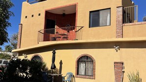 Um edifício de dois andares com piscina, varanda com telhado de palha e área de pátio com móveis de exterior.