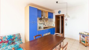A compact kitchen with blue cabinets, a wooden dining table, and a colorful sofa.