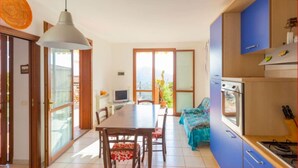 A modern kitchen with blue cabinets, a dining area with a table and chairs, and a large window with a view of greenery.