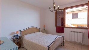 A bedroom with a bed, bedside table, lamp, and a window with a view of a building.