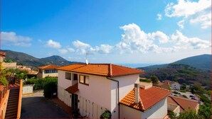 A residential area with a house featuring a tiled roof, a satellite dish, and a view of surrounding hills.