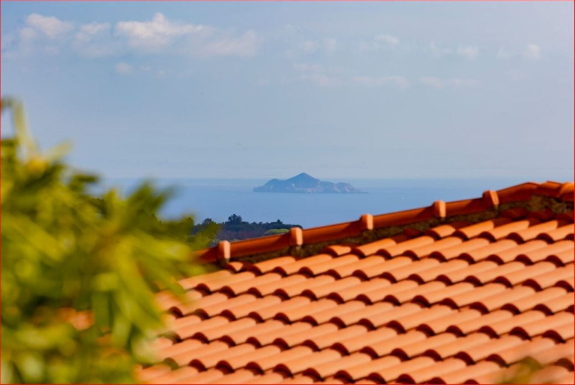 A coastal view with a tiled roof and a distant island.