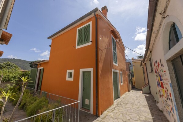 Un estrecho callejón con un edificio y contraventanas pintadas de naranja y verde.