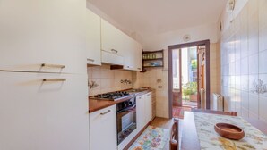 A compact kitchen with white cabinets, a wooden countertop, and a stove. There is a small window and a door leading to an outdoor area.