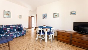 A living room with a sofa, dining table, chairs, a TV, and a wooden cabinet.