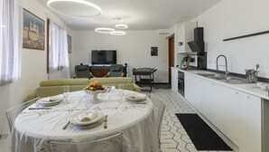 Eine moderne Küche mit Essbereich, mit einem runden Tisch für vier Personen, einer Couch und einem Fernseher im Hintergrund.