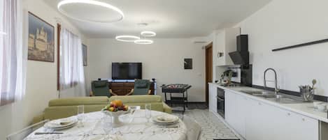 A modern kitchen with a dining area, featuring a round table set for four, a sofa, and a TV in the background.