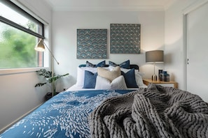Une chambre à coucher comprenant un lit, une lampe de chevet, une plante et deux œuvres d’art murales.