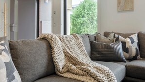 Ein Wohnzimmer mit einer Couch, einer Strickdecke und Blick auf Grün.