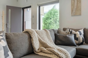A living room with a sofa, a knitted blanket, and a view of greenery outside.