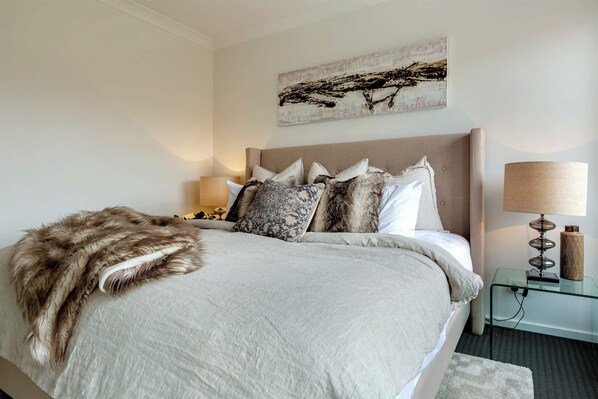A neatly made bed with a fluffy throw, a bedside lamp, and a wall-mounted abstract painting.