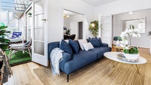 Un salon moderne avec un canapé bleu, une table basse ronde et une vue sur un balcon, accessible par une porte vitrée.