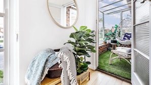 Une pièce accueillante avec un grand miroir, une plante en pot, un banc rembourré et une vue sur un jardin par une porte ouverte.