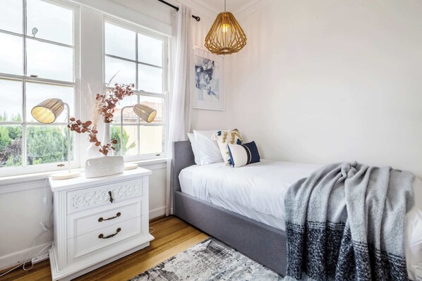 A bedroom with a bed, bedside table, lamp, and a window with a view.