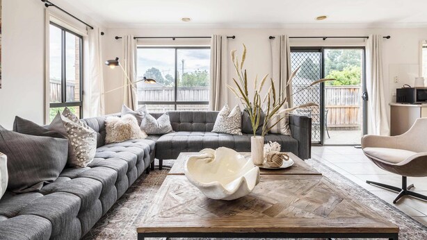 A modern living room with a sectional sofa, a coffee table, and a view through large windows.