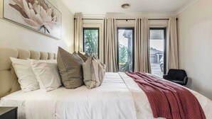 A hotel room with a large bed, a window with curtains, a chair, and a painting on the wall.