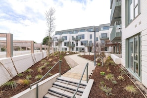 A modern building with a courtyard, steps leading to a wooden deck, and a pathway.