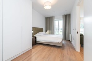 A modern bedroom with a bed, bedside table, lamp, and a view of the outdoors through large windows.