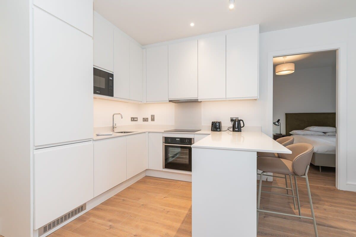 A compact kitchen with white cabinets, a microwave, an oven, and a small island with stools.