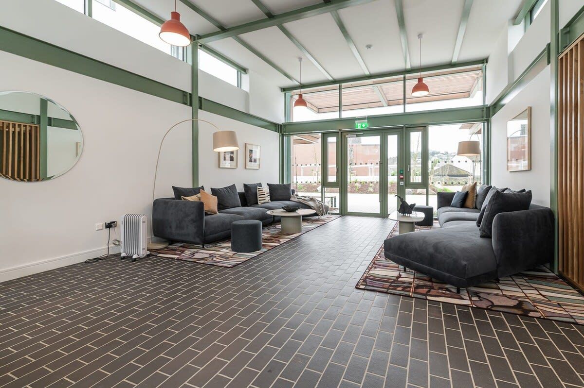 A spacious lobby with a brick floor, grey sofas, and a large mirror.