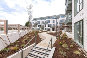 A modern apartment building with a central courtyard, outdoor seating area, and a staircase leading to the entrance.