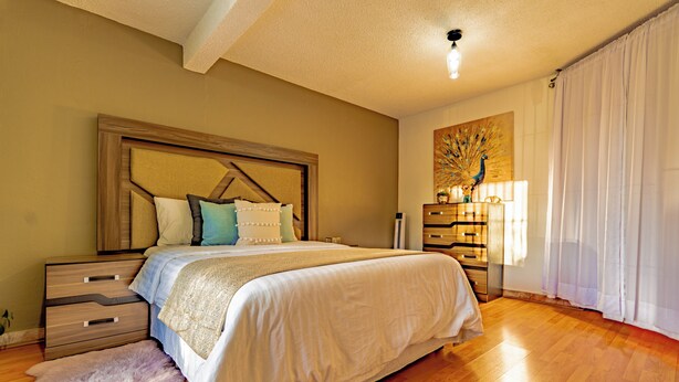 A bedroom with a large bed, wooden nightstands, a fluffy rug, and a decorative tree painting. - Residencia en la Ciudad de Oaxaca (Oaxaca)