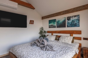 A bedroom with a large bed, a wooden headboard, a wall-mounted TV, and three framed artworks. - Vineyard Cottage Sunny Hill (Trebnje)