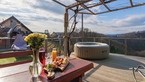 Eine Holzterrasse mit Esstisch, einem Whirlpool und einem schönen Ausblick auf die Hügel.