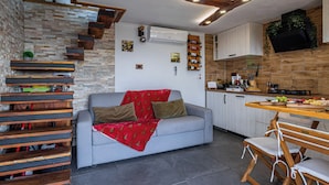 Eine gemütliche Küche mit grauem Sofa, Holzregalen und einem Essbereich mit Holztisch und Stühlen.