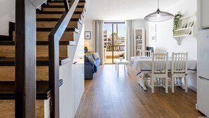 A modern kitchen with a dining area, wooden staircase, and large windows offering a view of buildings.