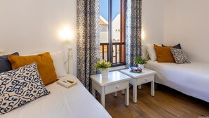 A room with two beds, a small table with books, and a window with patterned curtains.