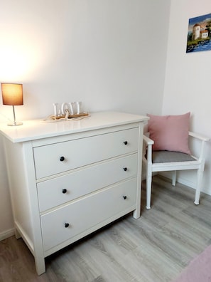 A white bedside table with drawers, a lamp, and a small decorative item.