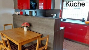 A modern kitchen with red cabinets, a wooden dining table, and a view of the outside.