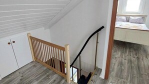 A room with a sloped ceiling, wooden flooring, a wooden staircase with a handrail, and a window with a view of the sky.