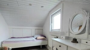 A bedroom with a sloped ceiling, a single bed, a vanity with a mirror, and a window.